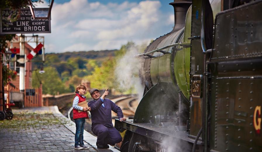 Photo of a young child and train driver looking at a steam engine