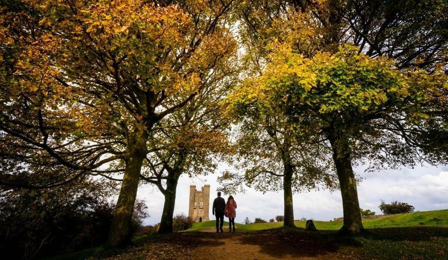 Photo of people waking towards Broadway Tower with Autumn colour on the trees