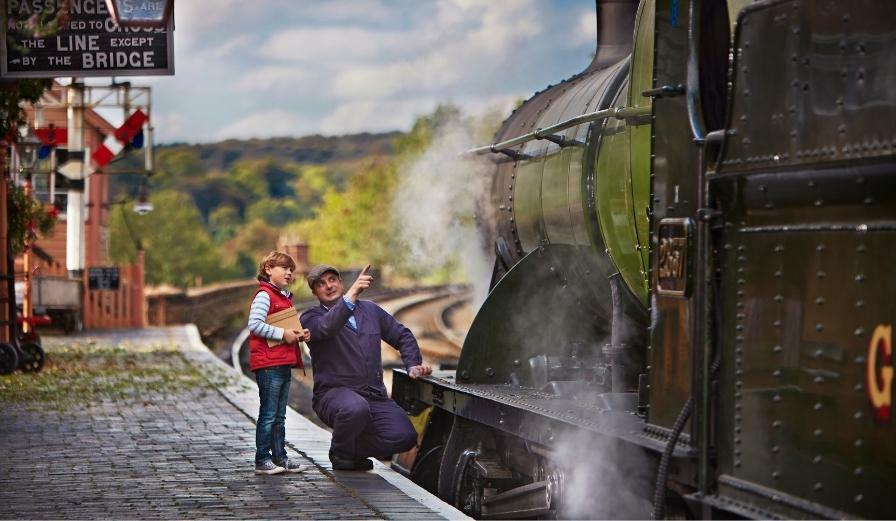 Photo of young child and train driver on platform at Severn Valley Railway pointing towards a steam train