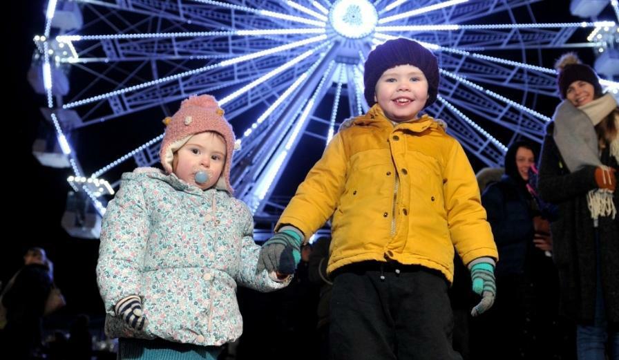 Photo of young childern holding hands with Ferris wheel in the background