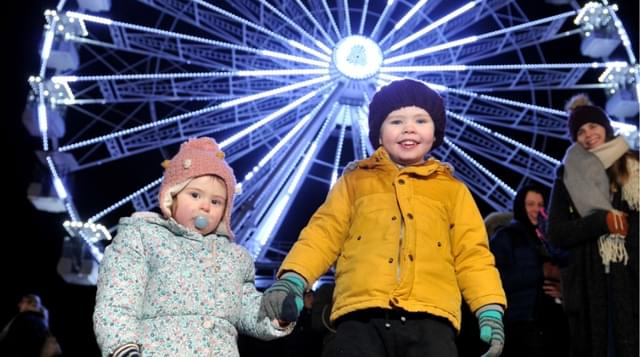 Photo of two children holding hands with Ferris wheel in the background